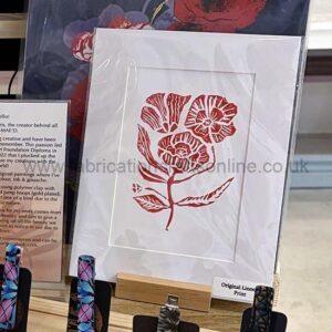 Red floral linocut print framed in plastic on display in a shop; label reads 'Original Linocut Print'.