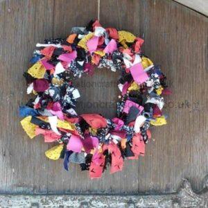 Colorful fabric patchwork wreath hanging on a weathered wooden door or surface/f hanging on door edge.