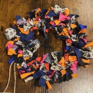 Colorful fabric-scrap wreath arranged in a circular shape on a wooden surface, with orange, pink, blue, and gray pieces.