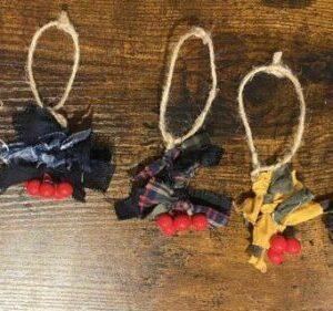 Five handmade fabric garlands with red berries, tied to twine loops on a wooden surface.