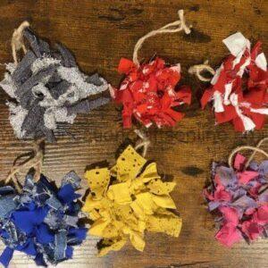 Six fabric pom-poms tied with twine, arranged on a wooden surface in gray, red, red-and-white, blue, yellow, and pink colors.