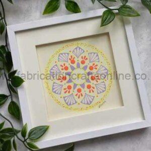 White square frame containing a pastel mandala design in yellow, purple, and pink, placed on a light surface with green leaves around.