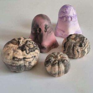 Five small gourds with two purple fabric ghost decorations on a white surface for Halloween decor.