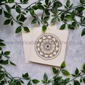 Two cream-colored cards feature a circular brown mandala design, placed on a light surface and surrounded by green ivy vines.