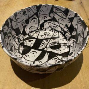 White paper bowl with a black-and-white collage of faces on a wooden table.