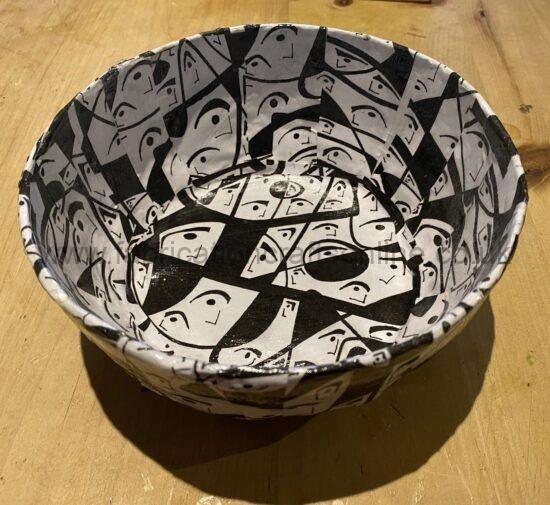 White paper bowl with a black-and-white collage of faces on a wooden table.