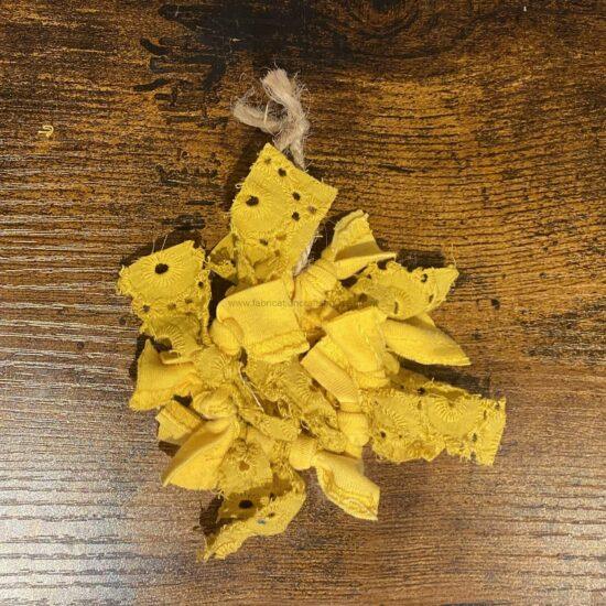 Yellow fabric scraps with embroidered daisy-like flowers on a dark, wooden surface; small torn pieces and frayed edges present on a rustic table layout.