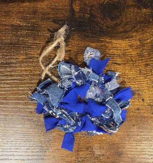 Blue denim fabric scraps tangled with frayed beige twine on a wooden tabletop.