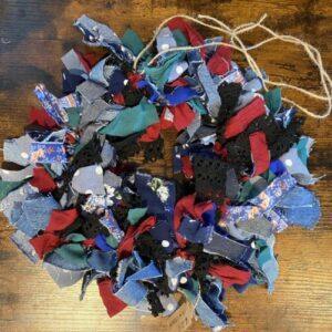 A bundle of colorful fabric scraps and lace tied with twine, arranged in a rough heart shape on a wooden surface.