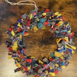 Colorful fabric fringe arranged in a circular wreath on a rustic wooden surface.