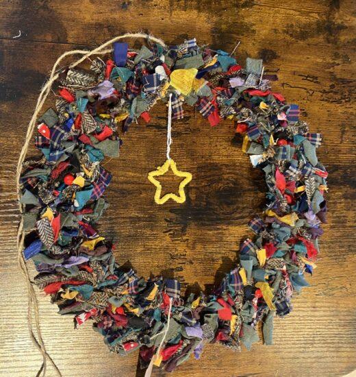 Colorful fabric scrap wreath hung on a dark wooden surface, with a yellow star charm at the bottom.