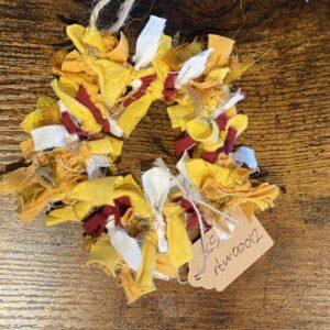 Multicolored fabric tassel hanging on a wooden surface with a jute loop and a paper price tag.