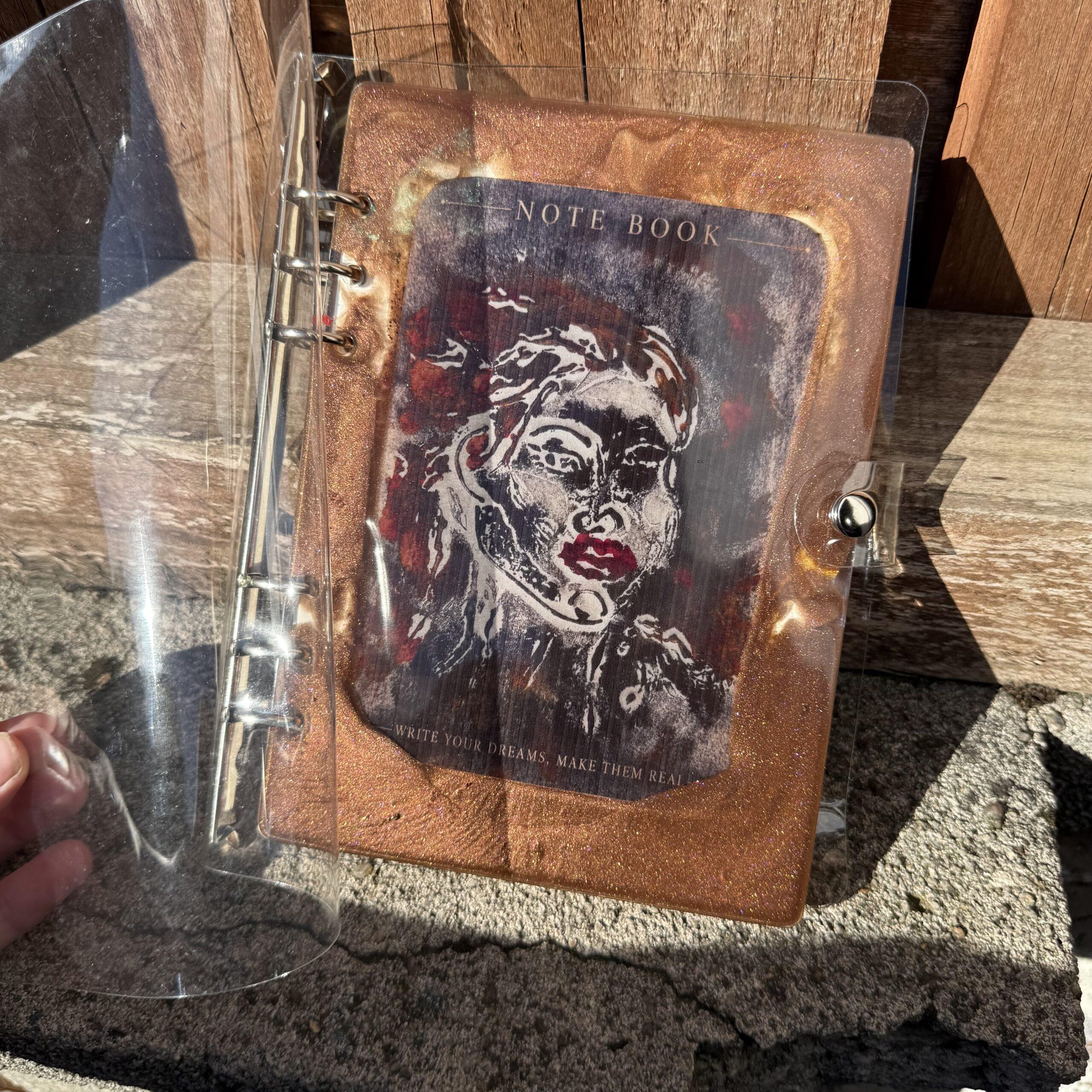 img handmade a refillable notebook featuring an original alova artwork set within a hand poured resin cover in warm copper tones with subtle colour details