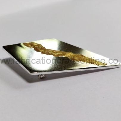 Close-up of a small rectangular silver plate with a gold foil smear on its surface, set against a white background.