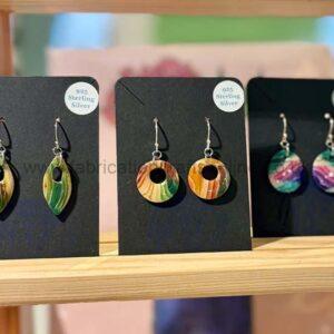 Colourful circular wooden earrings with a central hole on black display cards, labelled 925 Sterling Silver, arranged on a wooden shelf