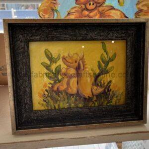 Framed painting of two yellow cartoon dogs playing in tall grass on a yellow background; black inner frame.