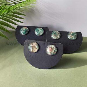Group of marbled green and pink stud earrings on black display cards.