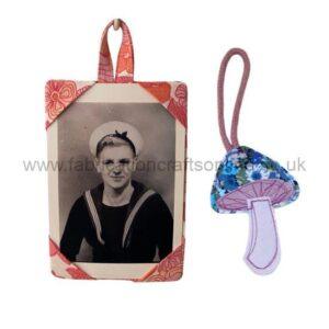 Small floral keepsake photo frame with a black-and-white portrait of a sailor woman, paired with a decorative mushroom-shaped charm on a string.