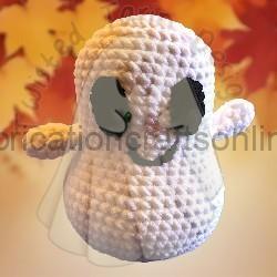 Small white crocheted ghost figure with closed eyes, wearing a sheer veil, set against a warm autumn background.
