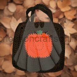 Black tote bag with an orange pumpkin applique on the front, set against a background of dried leaves.