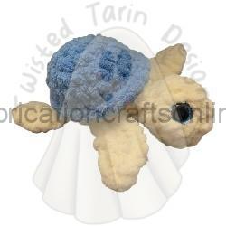 Soft beige plush turtle with a blue shell resting on a white ruffled surface.