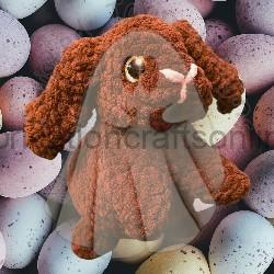 Brown plush dog toy with floppy ears sits in front of pastel speckled Easter eggs in the background.