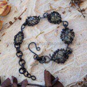 Handcrafted bracelet with black wire-wrapped dark-green stones and a hook clasp on a light fabric background.